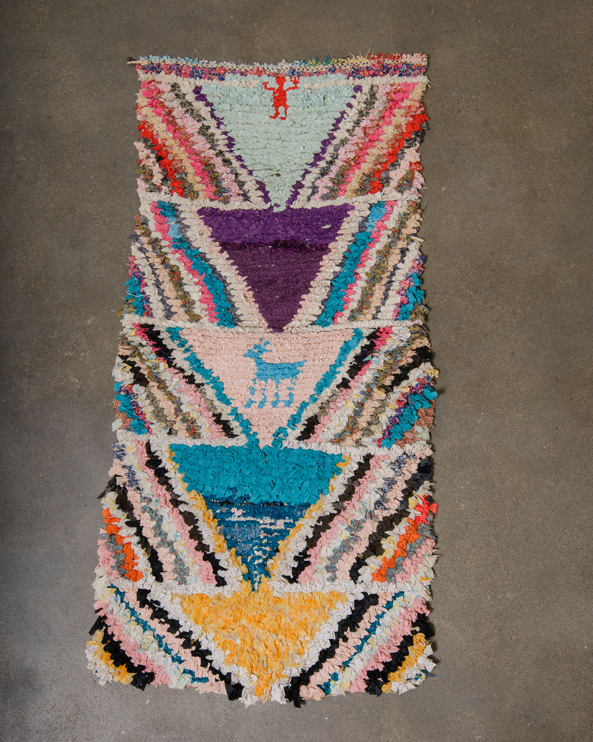Berberlin boucherouite runner rug featuring blue, purple, yellow and pink, laying on a grey concrete floor.